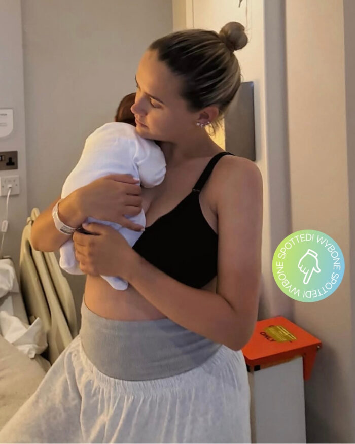 Molly-Mae Hague standing in a hospital room while holding her newborn baby. A Wybone clinical waste sack holder is visible beside the hospital bed in the background, alongside other medical equipment.